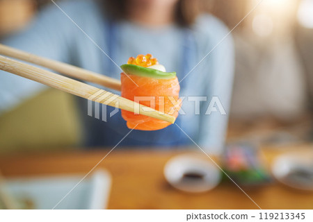 Sushi, eating food and hand with chopsticks at restaurant for nutrition and health. Closeup of a person with wooden sticks for dining, Japanese culture and salmon cuisine with creativity on fish 119213345