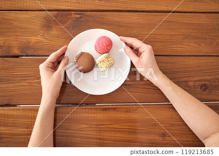 Hands holding white plate with assorted macarons on rustic wooden table Hands holding white plate with assorted macarons on rustic wooden table 119213685