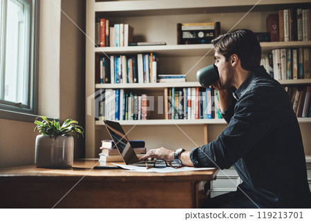 Caffeine keeps me going on my busy days. Shot of a handsome young businessman drinking coffee while working on a laptop in his home office. 119213701