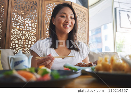 Asian, food and woman at a restaurant eating for dinner or lunch meal using chopsticks and feeling happy for nutrition. Plate, young and person enjoy Japanese cuisine, noodles or diet at a table 119214267