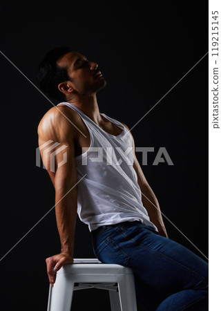 Sexy, muscle and man on chair in studio with fitness inspiration, beauty aesthetic and sensual fashion. Erotic art, sexual body and male model sitting on black background, thinking in dark lighting. 119215145