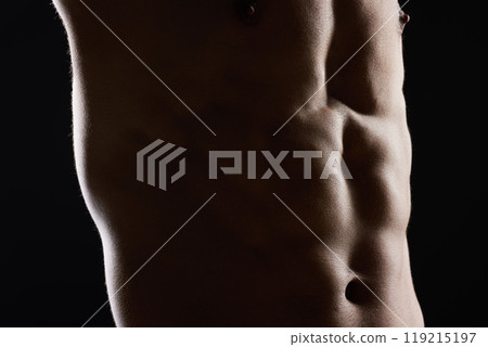 Man, abdomen and muscle in dark studio, shadow and wellness with health, strong and workout by black background. Bodybuilder guy, shirtless and stomach with skin, aesthetic and power in dark for art Man, abdomen and muscle in dark studio, shadow and wellness with health, strong and workout by black background. Bodybuilder guy, shirtless and stomach with skin, aesthetic and power in dark for art 119215197