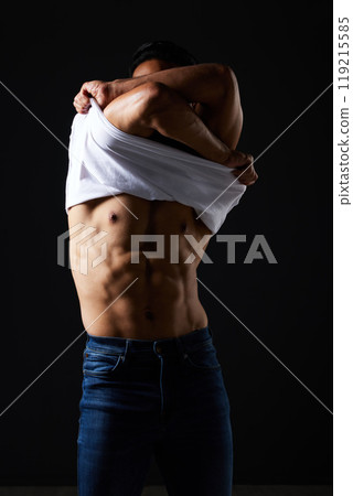 Muscle, body and man take off tshirt to show skin and stomach for wellness, workout and training in studio. Bodybuilder, exercise and man remove t-shirt for strong abs and fitness on black background 119215585