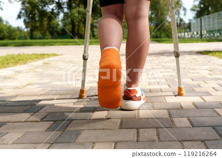 Person walking with crutches and a cast on their leg outdoors 119216264