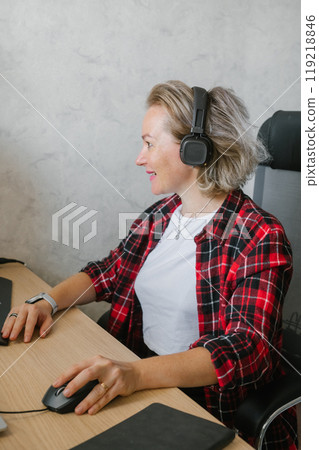 Mature Woman with Headphones Working at Computer Desk 119218846
