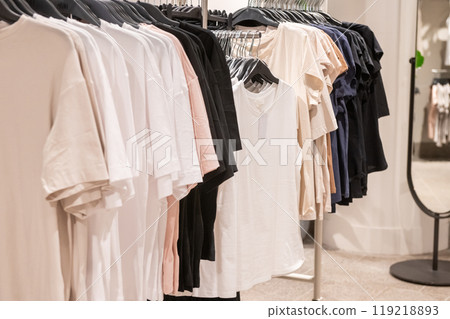 Various t-shirts in neutral colors on hangers in retail clothing store. 119218893