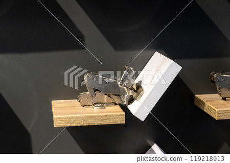 Metal hinge mechanism on wooden block displayed against dark background. Metal hinge mechanism on wooden block displayed against dark background. 119218913