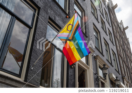 Progress Pride flag with intersex symbol displayed on a building facade in an urban street. Progress Pride flag with intersex symbol displayed on a building facade in an urban street. 119219011