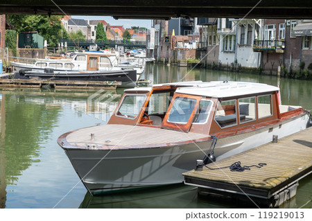 Small wooden boat docked in a peaceful canal surrounded by historic buildings. Small wooden boat docked in a peaceful canal surrounded by historic buildings. 119219013