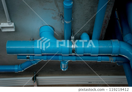 A bright blue pipes attached to a solid concrete wall 119219412