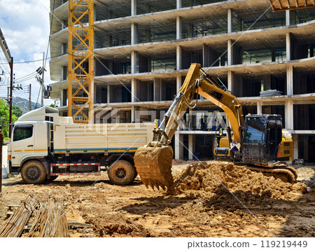 Excavator loads ground into a dump truck at a construction site 119219449