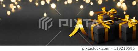 Three elegant black gift boxes with gold ribbons on a black background 119219596