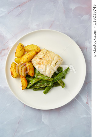 Delicious baked cod fillet served with seasoned potatoes and green beans on a white plate 119219749