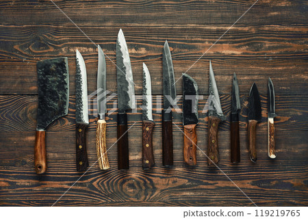 A collection of various kitchen knives displayed on a rustic wooden table 119219765