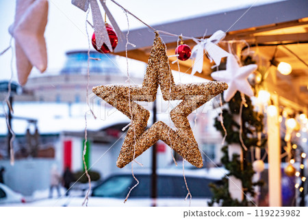 Stylish christmas golden star illumination and fir branches with red and gold baubles, golden lights bokeh on front of building at holiday market in city street.Christmas street decor 119223982