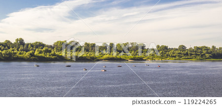 There are many small boats with fishermen along the riverbank, overgrown with trees, early summer morning 119224265