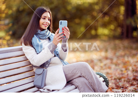 A girl with a smartphone takes photos in an autumn forest A girl with a smartphone takes photos in an autumn forest 119226014