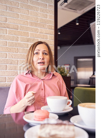 Surprised woman in cafe enjoying coffee and dessert against brick wall backdrop Surprised woman in cafe enjoying coffee and dessert against brick wall backdrop 119226723