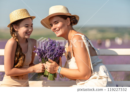 A woman and a child are sitting on a bench in a field of purple flowers lavande. The woman is holding a bouquet of flowers and the child is holding a bouquet of flowers as well A woman and a child are sitting on a bench in a field of purple flowers lavande. The woman is holding a bouquet of flowers and the child is holding a bouquet of flowers as well 119227332