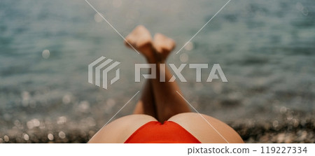 A woman sunbathes on the beach, lying on her stomach in a red swimsuit against the sea backdrop. A woman sunbathes on the beach, lying on her stomach in a red swimsuit against the sea backdrop. 119227334