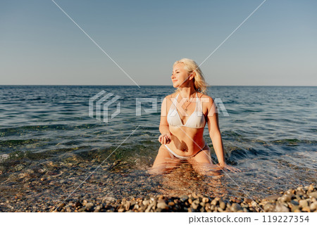 A woman in a bikini is sitting in the ocean 119227354