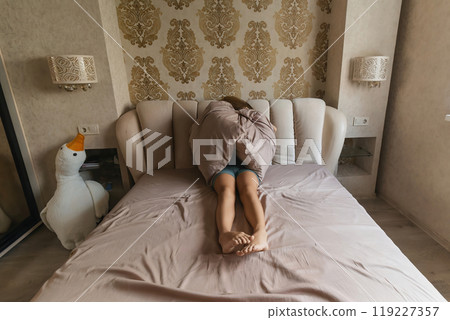 A girl is laying on a bed with pillows and a stuffed duck. She is looking at the camera with a sad expression. A girl is laying on a bed with pillows and a stuffed duck. She is looking at the camera with a sad expression. 119227357