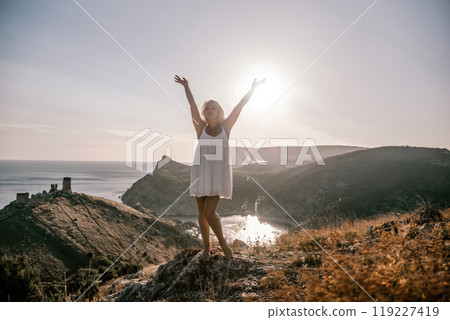 woman standing hill with her arms raised in the air, looking up at the sun. The scene is peaceful and serene, with the woman's expression conveying a sense of joy and happiness. woman standing hill with her arms raised in the air, looking up at the sun. The scene is peaceful and serene, with the woman's expression conveying a sense of joy and happiness. 119227419