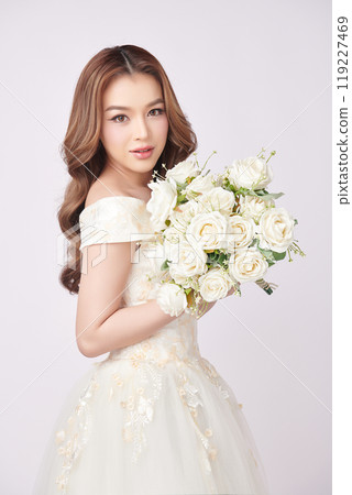 Beautiful young asian woman in wedding dress holding bouquet on white background, 119227469