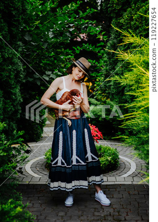 Woman is holding a chicken in a lush green garden 119227654