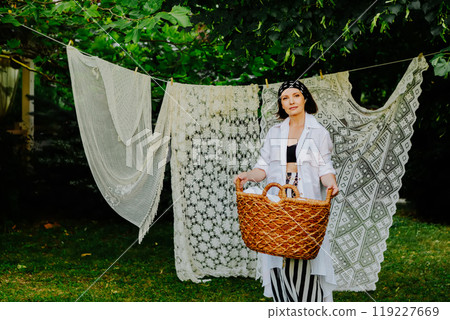 Woman stands in a lush green garden, hanging intricate lace fabric on a clothesline Woman stands in a lush green garden, hanging intricate lace fabric on a clothesline 119227669