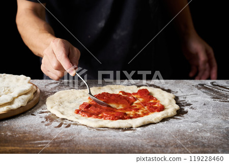 披薩廚師將番茄醬塗在披薩麵團上 披薩廚師將番茄醬塗在披薩麵團上 119228460