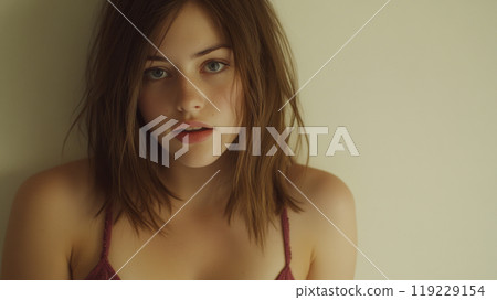 Young woman with tousled hair gazes softly against a neutral background in a cozy indoor setting 119229154