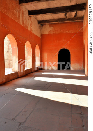 Empty historic room with orange walls and arches casting shadows in midday light 119229179