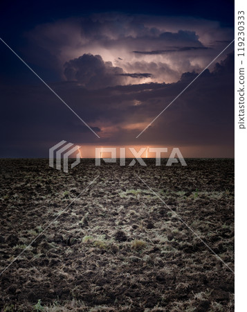 Powerful lightnings in dark stormy sky above plowed farm field 119230333