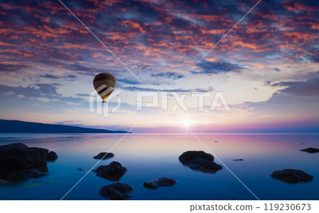 Hot air balloon flies in glowing sunset sky above calm sea Hot air balloon flies in glowing sunset sky above calm sea 119230673