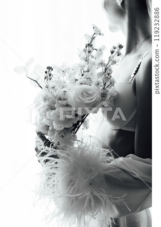 The morning of the bride, a woman wearing a white silk robe holds a wedding bouquet. Close-up photo. 119232886
