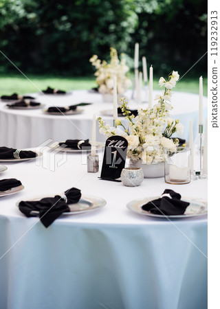 Outdoor wedding banquet. The tables are covered with tablecloths. There are various accessories and plates with napkins on the tables. Outdoor wedding banquet. The tables are covered with tablecloths. There are various accessories and plates with napkins on the tables. 119232913