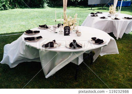 Outdoor wedding banquet. The tables are covered with tablecloths. There are various accessories and plates with napkins on the tables. Outdoor wedding banquet. The tables are covered with tablecloths. There are various accessories and plates with napkins on the tables. 119232986