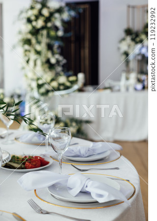 Luxurious restaurant. Luxurious interior, white tables, serving dishes and glasses for guests Luxurious restaurant. Luxurious interior, white tables, serving dishes and glasses for guests 119232992