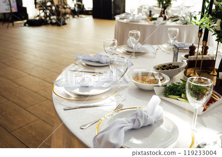 Luxurious restaurant. Luxurious interior, white tables, serving dishes and glasses for guests Luxurious restaurant. Luxurious interior, white tables, serving dishes and glasses for guests 119233004
