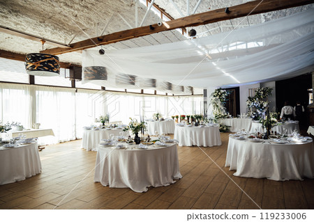 Luxurious restaurant. Luxurious interior, white tables, serving dishes and glasses for guests Luxurious restaurant. Luxurious interior, white tables, serving dishes and glasses for guests 119233006
