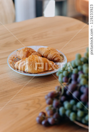 Fresh croissants on a plate, served with grapes on a wooden table for a perfect breakfast Fresh croissants on a plate, served with grapes on a wooden table for a perfect breakfast 119233923
