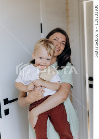 Smiling mother holding her happy child indoors, capturing a joyful family moment Smiling mother holding her happy child indoors, capturing a joyful family moment 119233930