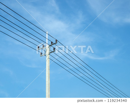 Reinforced concrete pillar with high-voltage wires against a clear blue sky. Transmission of electricity by wires over long distances. Electricity power lines against a clear sky. 119234340