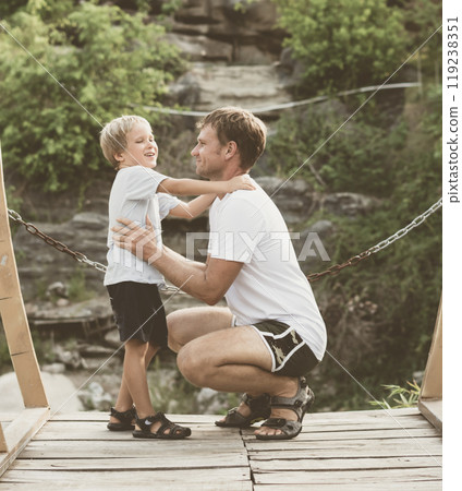 Vintage matte effect photo. Happy lifestyle moment. Man crouched, gesture hand, attentive listen boy walk funny play. Father hug hold touch child son closely in arms embrace, fatherhood love affection 119238351