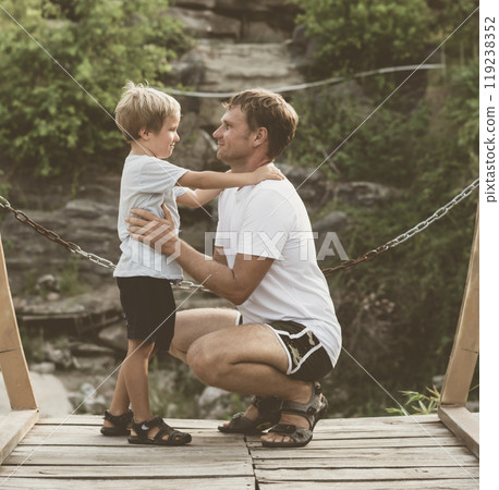 Vintage matte effect photo. Happy lifestyle moment. Man crouched, gesture hand, look into eyes each other listen boy walk funny play. Father hug hold child son closely arm embrace, fatherhood love 119238352