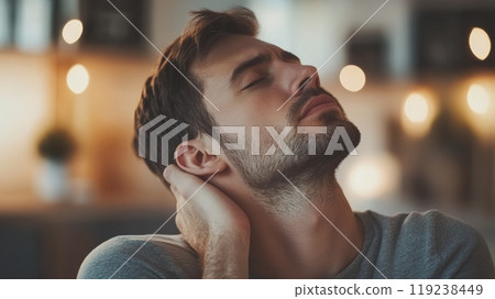 Young man is having a neck pain, touching the back of his neck, trying to relieve the ache. He is keeping his eyes closed 119238449
