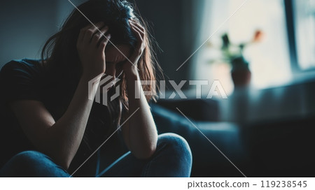 Young woman sits on the floor, holding her head in her hands, struggling with depression and anxiety, overwhelmed by sadness, loneliness, and stress 119238545