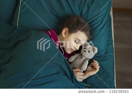 7 year old girl in red pajamas sleeps in green bed with her teddy bear toy 119238561