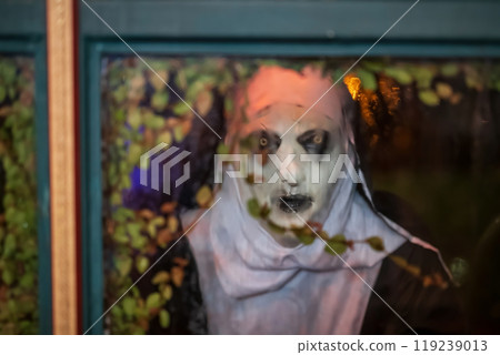Scary devilish nun look through window from outside at night 119239013